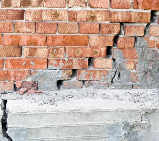 Pęknięta ceglana ściana i betonowy cokół, wskazujące na podbijanie fundamentów.