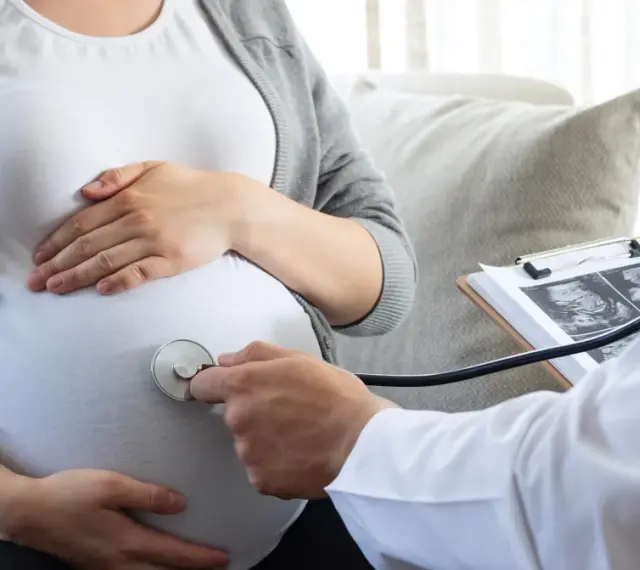 Lekarz osłuchuje brzuch ciężarnej, analizując wyniki badań USG. W trosce o zdrowie dziecka, wyklucza się m.in. cytomegalię.