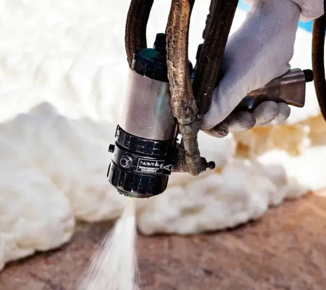 Ręka w rękawicy trzyma pistolet do natrysku pianki. Ocieplanie pianką cena za m2 jest kluczowa przy wyborze wykonawcy.