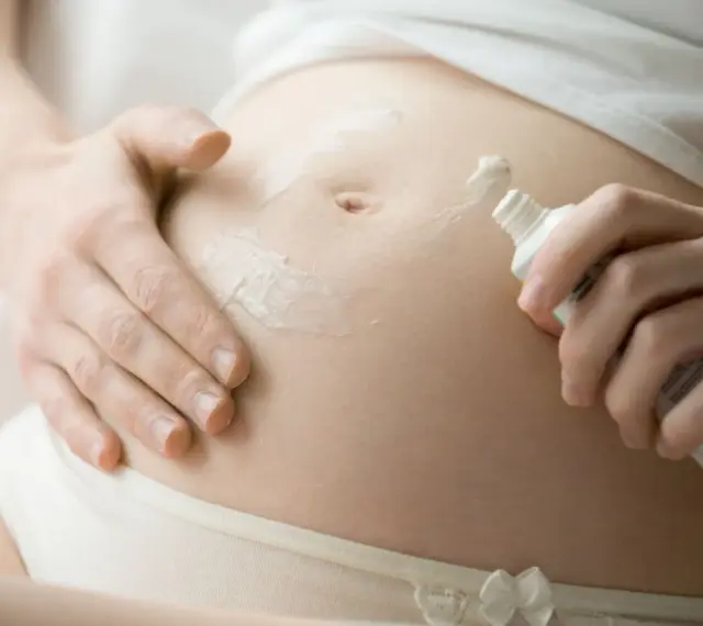 Kobieta smaruje brzuch w ciąży kremem, dbając o skórę. Pielęgnacja to klucz do tego, czym smarować brzuch w ciąży.