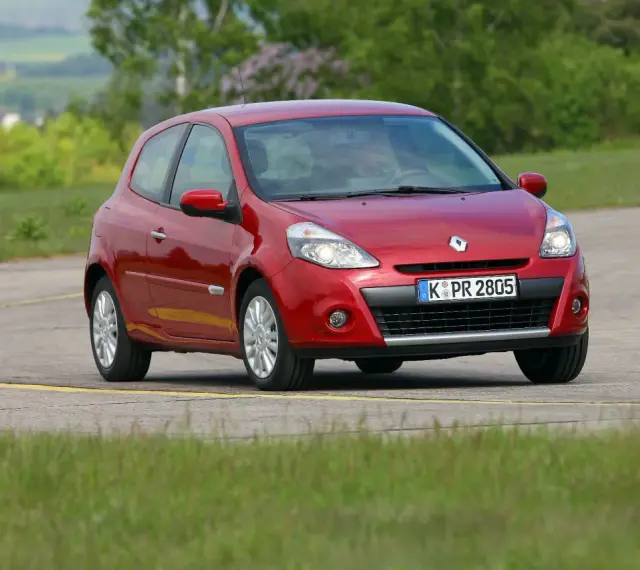 Czerwony Clio 3 na zakręcie drogi, otoczony zielenią.
