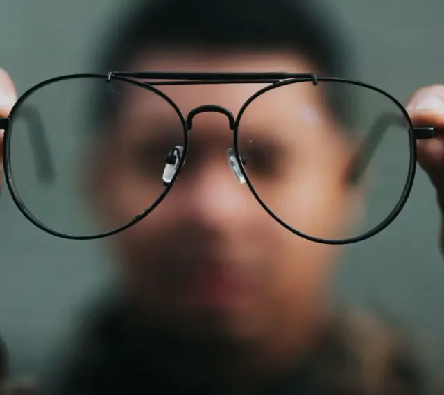 Osoba trzyma przed twarzą okulary, które sprawiają, że świat wygląda inaczej. Nowe okulary dziwne widzenie.