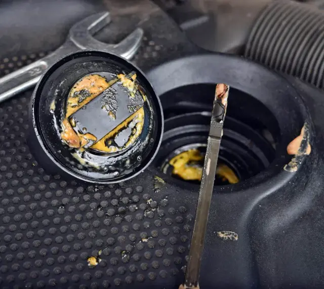 Osad na korku i bagnecie sugeruje konieczność wymiany uszczelki pod głowicą. Widoczne narzędzia wskazują na prace mechaniczne.