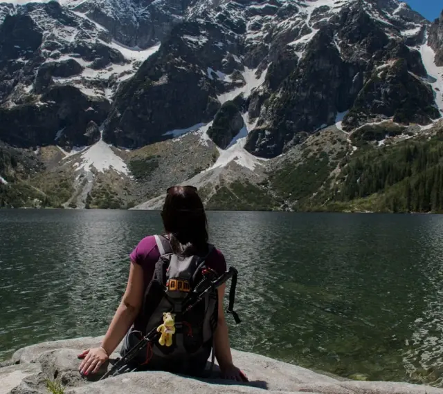 Widok na Morskie Oko z perspektywy turystki. Góry pokryte śniegiem, las i tafla jeziora tworzą malowniczą trasę.