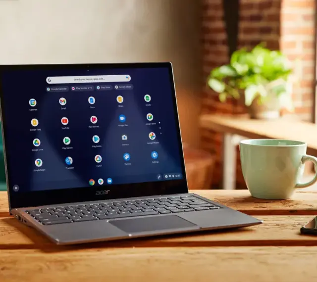 Laptop z systemem Chrome OS Flex, gotowy do pobrania, na drewnianym stole obok kubka i kluczy.
