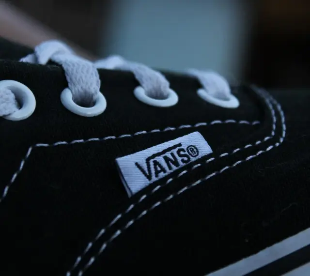 Zbliżenie na czarny but Vans z białymi sznurówkami i charakterystyczną metką. Vans to kultowa firma obuwnicza.