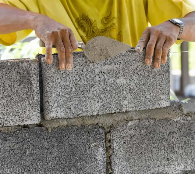 Ręce murarza układają bloczki betonowe fundamentowe, tworząc solidną podstawę.