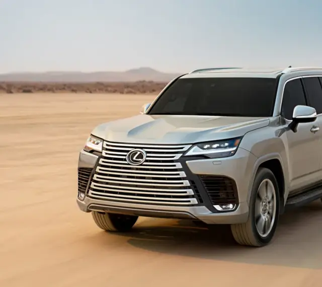 Srebrny Lexus LX 600 przemierza pustynię, zostawiając ślady na piasku.