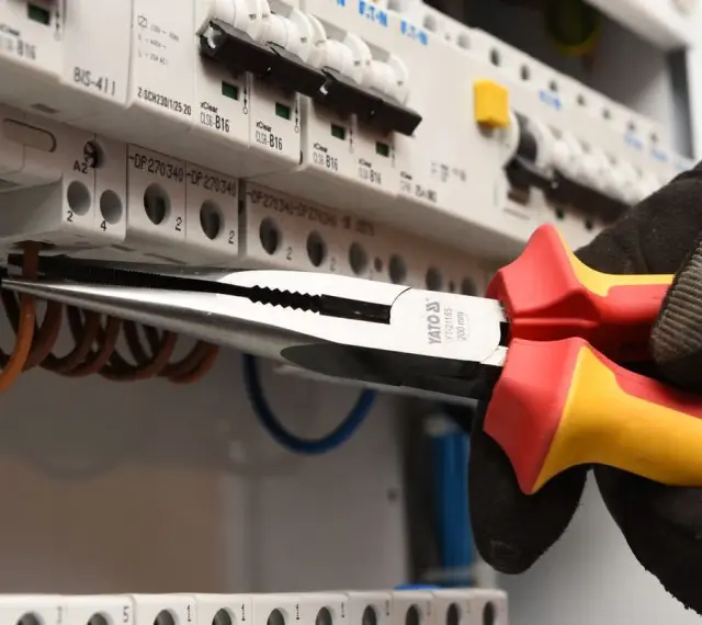 Elektryk w rękawicy wymienia instalację elektryczną, używając kombinerki do przewodów w skrzynce z bezpiecznikami.