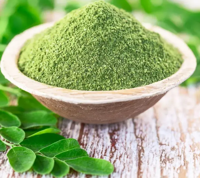 Zielony proszek z liści moringa w drewnianej miseczce, otoczony świeżymi liśćmi. Czy to ściema? Nie, to superfood!
