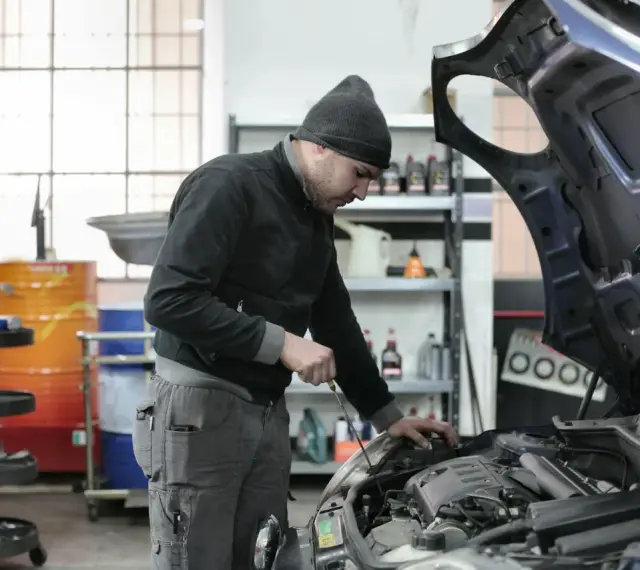 Mechanik w czapce z daszkiem sprawdza silnik. Zastanawiasz się, ile zarabia mechanik? Praca wymaga precyzji i wiedzy.