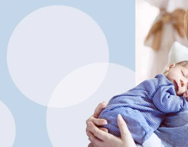 Uśmiechnięta mama tuli śpiącego noworodka w pasiastym pajacyku. Wskazówki, jak ubierać noworodka w domu.