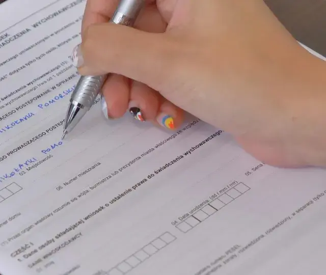 Ręka wypełnia kwestionariusz osobowy, wpisując dane dotyczące świadczenia wychowawczego.