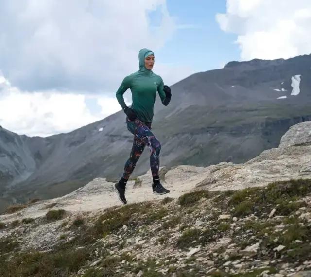 Kobieta w sportowym hidżabie biegnie po górskim szlaku, doskonaląc swoją kadencję w bieganiu.