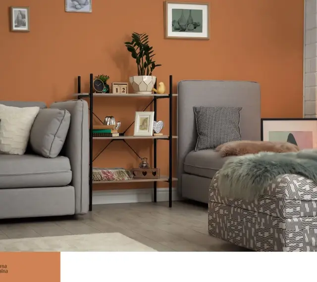 Przytulny salon z sofą i fotelem, ściany w ciepłym, **kolorze ceglastym**, regał z dekoracjami.