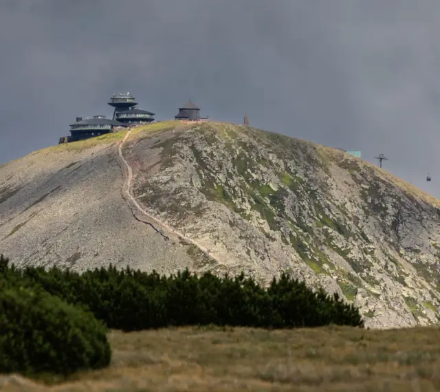 Schronisko i obserwatorium na szczycie w Karkonoszach, z widoczną kolejką linową i kamienistym zboczem.