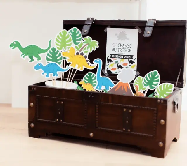 Coffre en bois rempli de décorations de dinosaures et de feuilles tropicales.