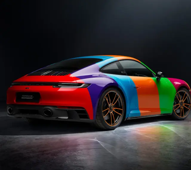 Porsche 911 Carrera GTS w tęczowym malowaniu, z pomarańczowymi felgami i odbiciami światła na podłożu.