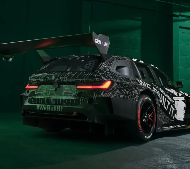 Wyścigowe BMW M3 2025 w kamuflażu, z ogromnym spojlerem i agresywnym dyfuzorem.