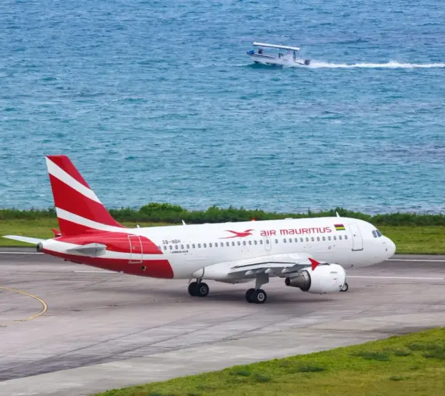 Samolot Air Mauritius na pasie startowym, w tle turkusowe morze i łódź. Twoje loty na Mauritius właśnie się zaczynają!