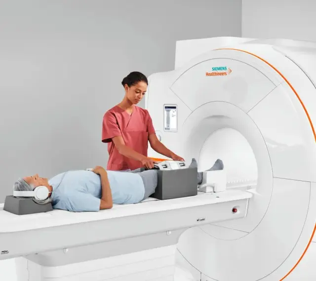 Pacjent leży na łóżku rezonansu magnetycznego, a technik przygotowuje jego nogi do badania. To właśnie mri co to za badanie, które pozwala zajrzeć do wnętrza ciała.