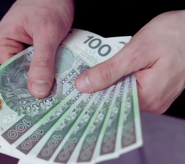 Dłonie trzymają stos banknotów 100 zł. Czy to wystarczy, by pokryć ile wynosi najniższa krajowa?