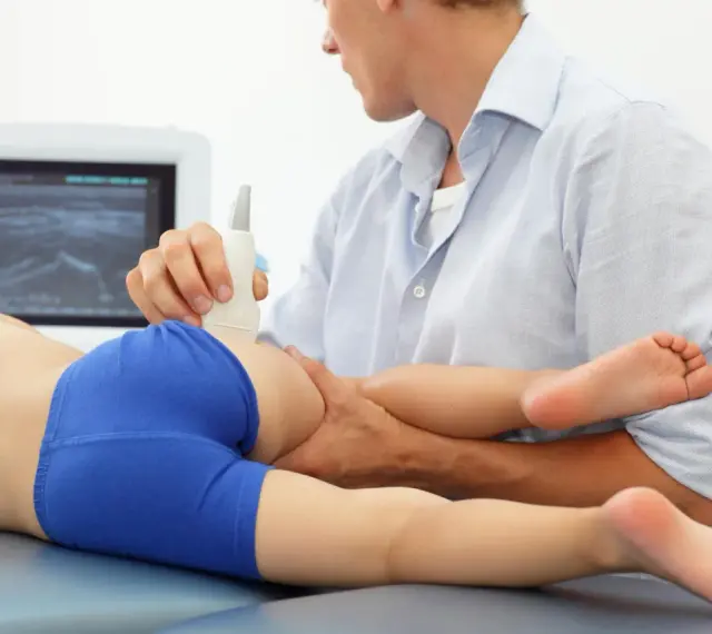 Lekarz wykonuje USG bioder u dziecka, diagnozując zapalenie stawu biodrowego.