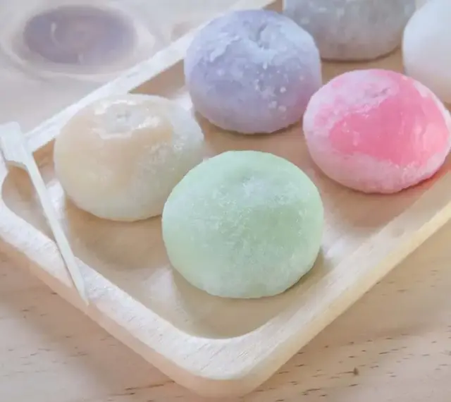 Kolorowe mochi na drewnianej tacce. Chcesz wiedzieć, jak zrobić mochi? Te słodkie kuleczki wyglądają pysznie!