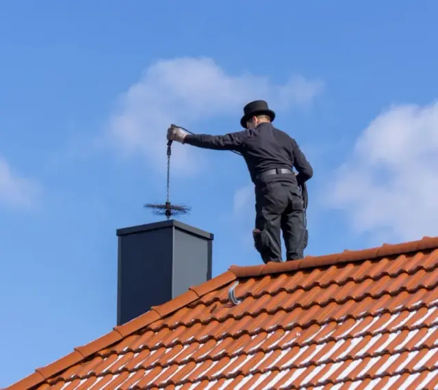 Kominiarz w cylindrze czyści komin na dachu. Sprawdź, jaka jest czyszczenie komina cena i zadbaj o bezpieczeństwo.