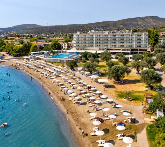 Piękna plaża na Evii, idealna na wycieczki fakultatywne. Hotel, basen, leżaki i mnóstwo ludzi kąpiących się w morzu.
