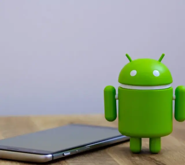 Zielony robot Android obok telefonu, symbolizujący najnowszą wersję systemu android 14.