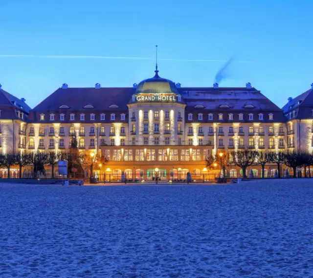 Elegancki Grand Hotel, część sieci luksusowych hoteli, lśni nocą na tle plaży.