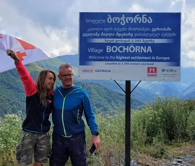 Para, z gruzińską flagą, na tle gór i znaku "Wioska Bochorna", najwyżej położona osada w Europie. Podróżując, warto zapytać: czy w Gruzji jest bezpiecznie?