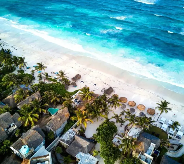 Rajskie wakacje w Meksyku: biała plaża, turkusowe morze i palmy otaczające urokliwe domki z krytymi dachami.