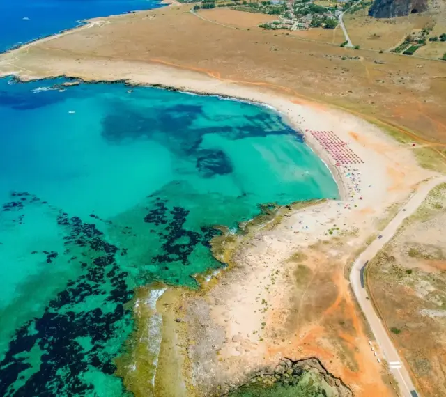 Widok z lotu ptaka na turkusowe morze i piaszczyste bari plaże z rzędami parasoli.