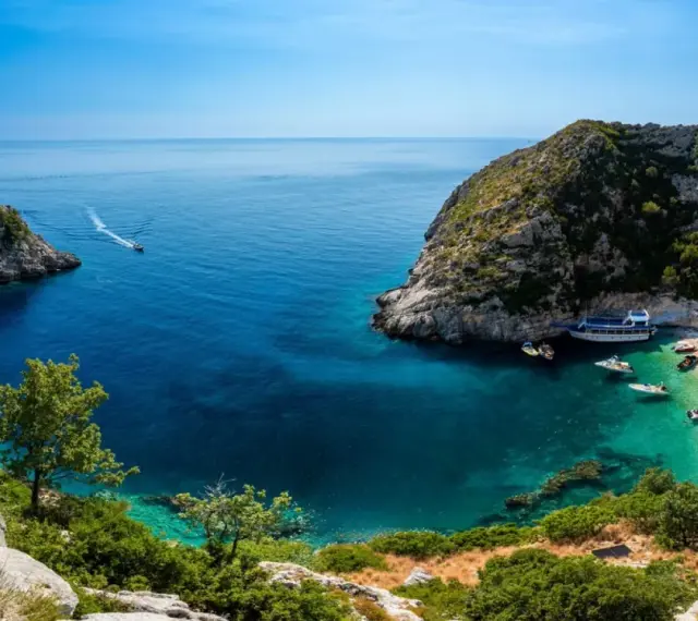 Malownicza zatoka z krystalicznie czystą wodą, plażą i łodziami. Idealne miejsce na wczasy samolotem all inclusive w Albanii.