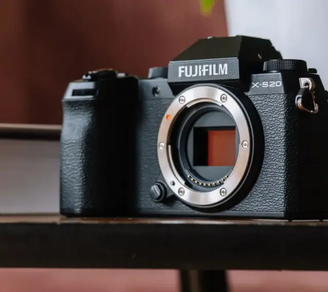 Czarny aparat Fujifilm X-S20 z obiektywem bez obiektywu, leżący na drewnianym stole obok książki.