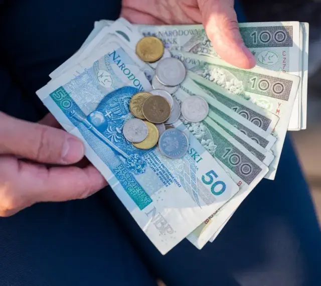 Ręce trzymają polskie banknoty 50 i 100 zł oraz monety. To może być kwota na bon oświatowy.
