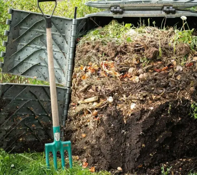Kompostownik pełen resztek organicznych, obok zielone widły. Proces kompostowania w ogrodzie, numer 200201.