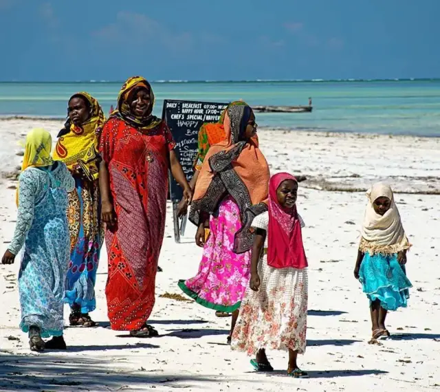 Kobiety w kolorowych strojach spacerują po plaży. Czy Zanzibar to państwo? Tak, to autonomiczny region Tanzanii, znany z pięknych plaż.