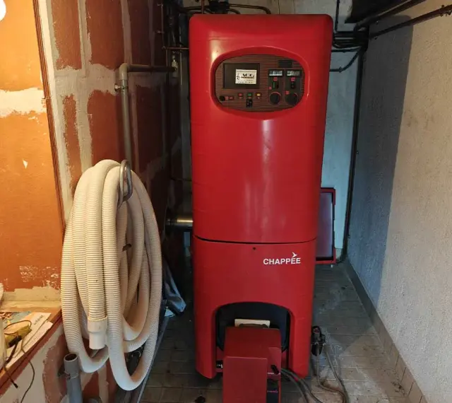 Chaudière rouge Chappée dans une pièce. Un tuyau blanc enroulé est accroché au mur. Pensez à l'assurance chaudière pour votre confort.