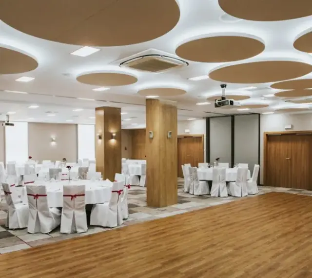 Elegancka sala bankietowa gotowa na wesele we wrześniu. Okrągłe stoły z białymi pokrowcami i czerwonymi wstążkami czekają na gości.
