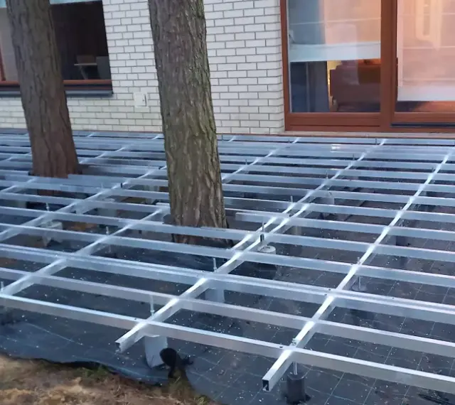 Konstrukcja pod wysoki taras z deski kompozytowej, z drzewami przechodzącymi przez ruszt.