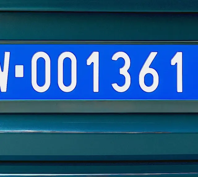 Niebieskie tablice rejestracyjne z numerem W-001361 na ciemnozielonym samochodzie.