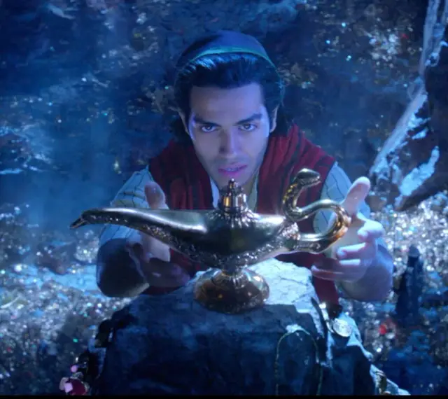 Aladyn, w mrocznej jaskini pełnej skarbów, trzymając magiczną lampę.