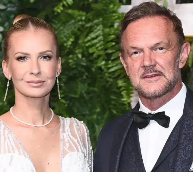 Cezary Pazura z żoną Edytą na ściance. Ona w białej, zdobionej sukni, on w eleganckim garniturze.