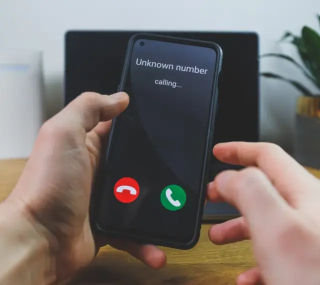 Dłoń trzyma telefon, na ekranie którego widnieje komunikat "Unknown number calling...". Czy odbierze, gdy numer prywatny dzwoni?