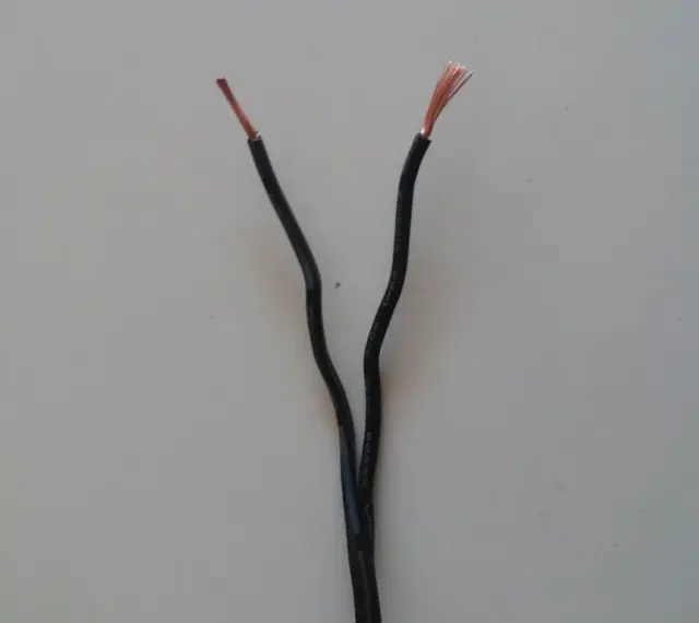Dwa czarne przewody elektryczne rozchodzą się, odsłaniając miedziane końcówki. Czy czerwony to plus czy minus?