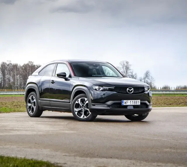 Czarna Mazda MX-30 na tle pochmurnego nieba i drzew.