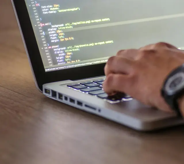 Kodowanie strony internetowej, widać fragment kodu HTML z listą nieuporządkowaną i rękę piszącą na klawiaturze.